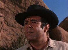 a man wearing a black cowboy hat standing in front of rocks