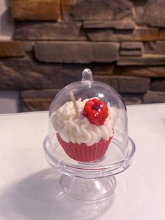 a cupcake with white frosting and a cherry on top is under a glass dome