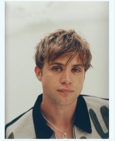 a close up of a person wearing a jacket and necklace with an interesting look on his face