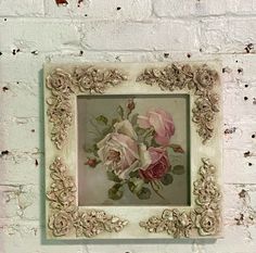 a painting hanging on the side of a white brick wall next to a vase with flowers in it