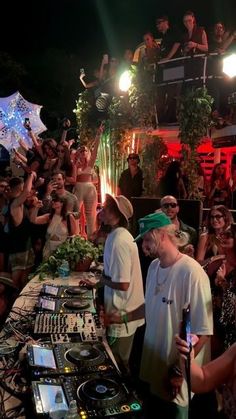 a group of people standing around a dj's set up at a party in front of a crowd