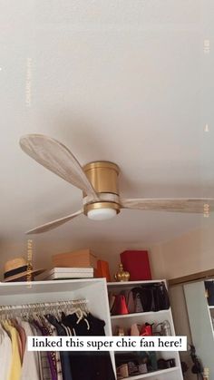 a ceiling fan that is hanging from the ceiling in a room with clothes on shelves