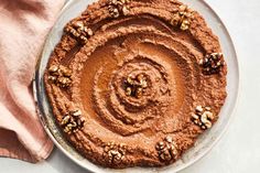 a chocolate cake with walnuts on top sitting on a plate next to a pink napkin