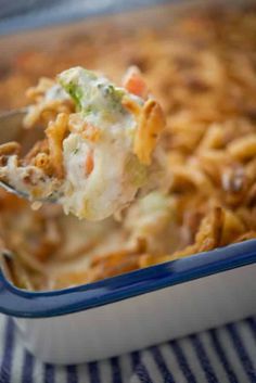 a spoon full of cheesy vegetable medley casserole in a blue dish