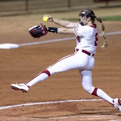 a female baseball player pitching a ball on top of a field with her mitt in the air