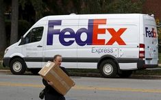 a man walking down the street with a box in his hand and a fed ex truck behind him