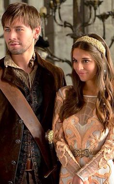 a young man and woman dressed in medieval costume standing next to each other, looking at the camera