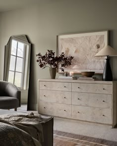 a bedroom with a dresser, chair and large window in the corner next to it