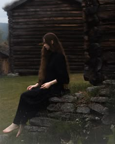 a woman sitting on top of a stone wall next to a log cabin