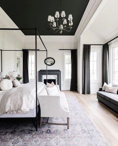 a bedroom with black and white walls, a canopy bed, chandelier, two couches and windows