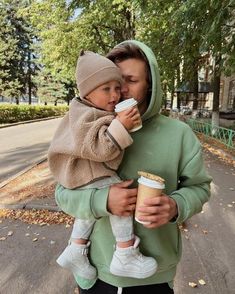 a man holding a child while wearing a hoodie and drinking from a coffee cup