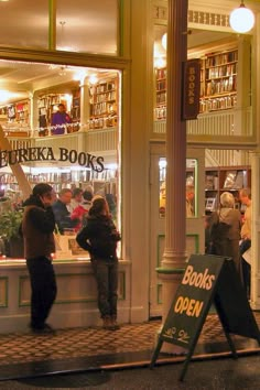 people standing in front of a book store with books on the shelves and an open sign