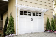 two white garage doors are open in front of a tan house with flowers and trees