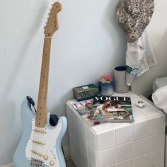 a blue guitar sitting on top of a white tiled floor next to a magazine rack