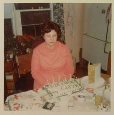 an old photo of a woman sitting in front of a birthday cake