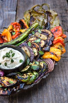 grilled vegetables on a platter with a dip in the middle and garnished with herbs