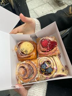 a person holding a box filled with different types of pastries in it's hands