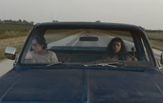 two people are driving in the back of a blue pickup truck down a country road