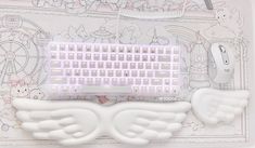 a white computer keyboard with angel wings on the front and back sides, surrounded by other items