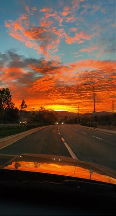 the sun is setting on an empty road with clouds in the sky and cars driving down it