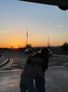 two people hugging each other in the middle of a parking lot as the sun sets