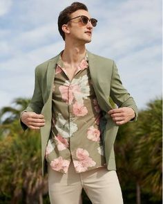 a man wearing sunglasses and a green jacket with pink flowers on it, standing in front of palm trees