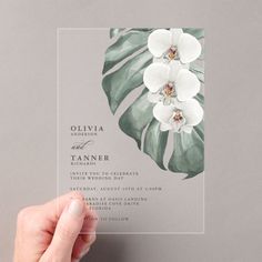 a person holding up a wedding card with flowers on the front and bottom, which are white in color