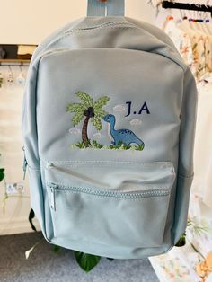 Dino backpack 🎒  Lots of colours available and loads of different designs. Any design requests please message and I'll happily accommodate.  These backpacks are fantastic as a changing bag, starting nursery, starting school. Adjustable straps and handy front pocket.  Designs are embroidered onto the front of the bag in any style/colour scheme of your choice. Child's name can be added. This embroidery is carefully crafted using the best quality threads 🧵 Time is taken to give you the very best Softback Bag For Back To School, Back To School Softback Bags, Softback School Bag For Back To School, Softback Bags For Students End Of School Year, Student Softback Bags For End Of School Year, Cute School Backpack Satchel, Cute School Satchel Backpack, Cute Satchel Backpack For School, Student Bags For Back To School