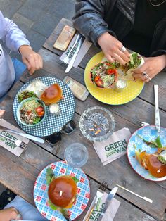 three people sitting at a picnic table with plates of food and drinks in front of them