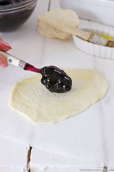 a person using a knife to spread black olives on dough