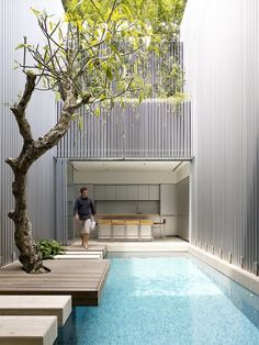 a man walking down the side of a building next to a tree and swimming pool