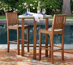 two wooden chairs and a table in front of a pool