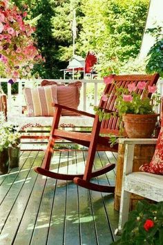 a wooden rocking chair sitting on top of a porch next to flowers and potted plants