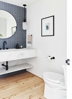 a white toilet sitting under a bathroom mirror next to a sink and a wooden floor