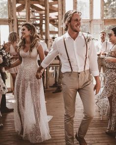 a man and woman holding hands walking down a wooden floor with other people in the background