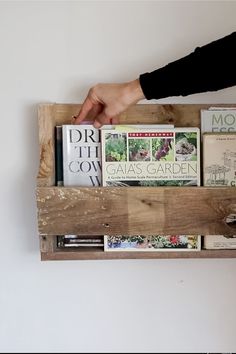 a person's hand is reaching for books in a wooden box on the wall