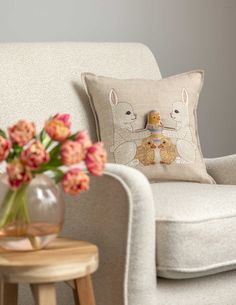 a white chair with flowers in a vase on it and a pillow sitting on the back