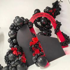 some black balloons and red flowers on a white table with a sign in the middle