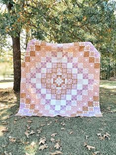 a pink and white quilt sitting on top of a grass covered field next to trees