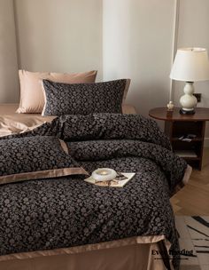 a bed with black and tan comforters in a bedroom next to a lamp on a table