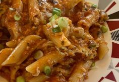 pasta with meat and vegetables in sauce on a red and white plate, sitting on a checkered tablecloth