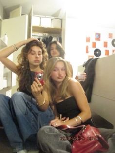 two young women sitting on the floor looking at their cell phones while another woman stands behind them