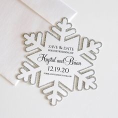 a white snowflake save the date card with silver foil on it's envelope