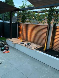 an outdoor patio with wooden slats and lights on the wall, surrounded by landscaping equipment