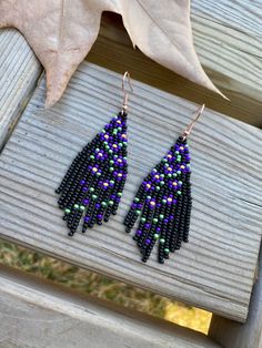 purple and green seed beaded earrings sitting on top of a wooden bench next to a leaf