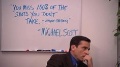 a man sitting at a desk in front of a whiteboard with writing on it