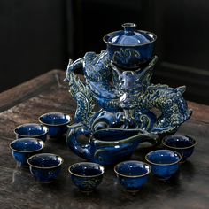 a blue and gold vase sitting on top of a wooden table next to nine cups