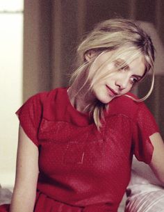 a woman in a red dress is sitting on a bed and looking at the camera