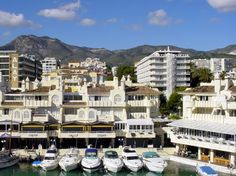 many boats are docked in the water next to some buildings and mountains behind them,