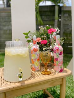 a wooden table topped with bottles and glasses filled with liquid next to a vase full of flowers